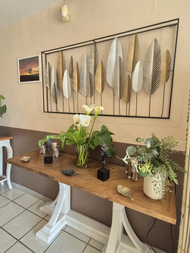 Console en bois décorée de bouquets de arums et d'eucalyptus sous une décoration murale en métal