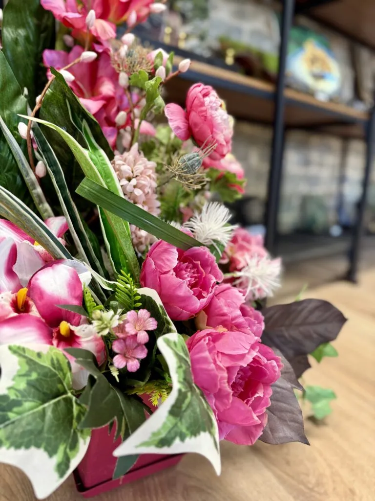 Gros plan sur un bouquet de pivoines artificielles roses et feuillage vert pour hommage funéraire